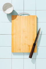 An empty cutting board, a Japanese knife and a small ceramic bowl on a blue tile background. The concept of cleanliness.