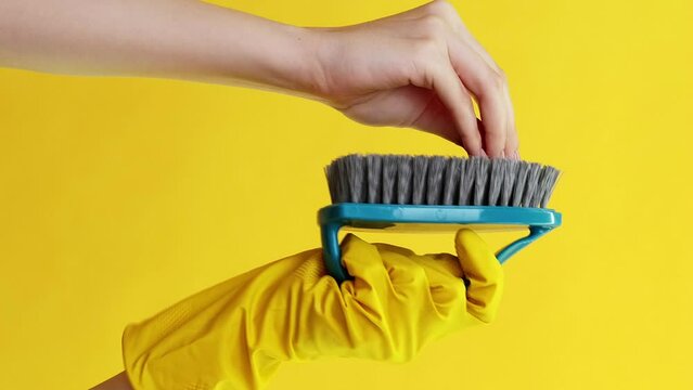 Vertical video. Cleaning equipment. Housework play. Arm in protective glove washing talking woman hand with blue brush isolated on yellow background.