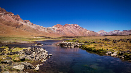 Hermoso arrollo que fluye del deshielo de Los Andes , vemos un gran ecosistema natural , con grandes texturas y un cielo muy azul.