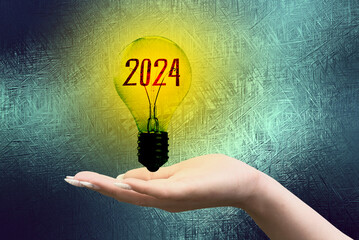 Eine Frau hält eine Glühbirne 2024 in der Hand - obrazy, fototapety, plakaty