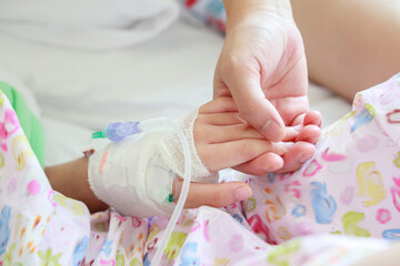 Mother holding child hand with saline IV solution in hospital