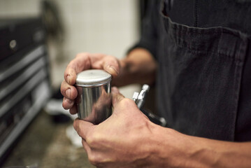 Hands of an unrecognizable young man closing the tank of a spray paint gun in his workshop. Close up view.