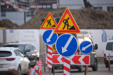 Roadworks warning traffic signs of construction work on city street and slowly moving cars