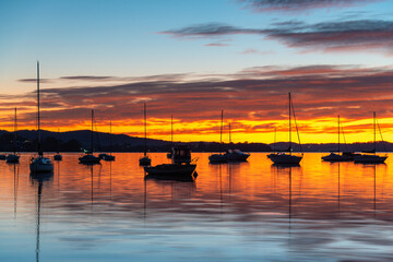 Fototapeta premium Sunrise over the water with boats, reflections and high cloud