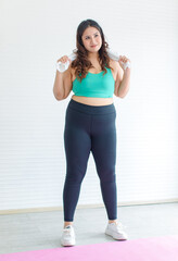 Closeup shot Asian young chubby fat healthy oversized overweight fit female sportswoman in sportswear sports bra legging standing smiling lifting dumbbells exercising training biceps in fitness gym