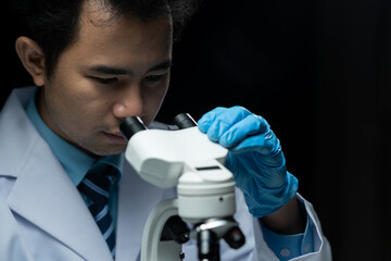 Asian scientist looking at a microscopic sample of experimental cyan is doing an in vitro vaccine...
