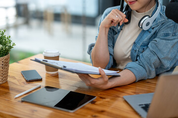 Young Asian businesswoman in headphones talking through microphone in studio, podcast, call center, customer service talking in video conference on laptop computer, tablet or meeting virtual office.