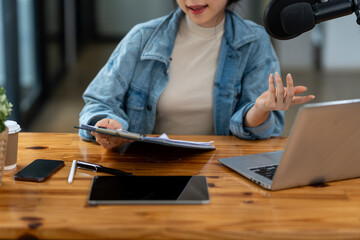 Young Asian businesswoman in headphones talking through microphone in studio, podcast, call center, customer service talking in video conference on laptop computer, tablet or meeting virtual office.