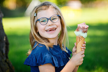 Happy preschool girl eating colorful ice cream in waffle cone on sunny summer day. Little toddler...