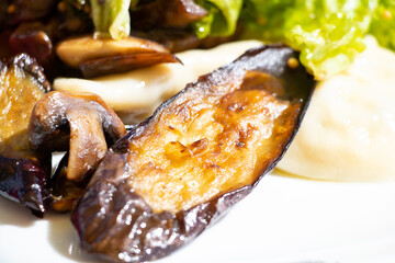 Cabbage leaves and mushrooms and a slice of fried eggplant on a white plate in the sun on the table, cooked vegetables for lunch