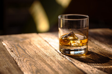 Glass with whisky with ice on a textured wooden table in harsh sunlight. - 649564831