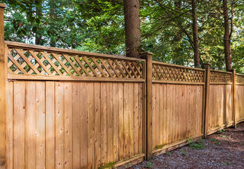 Nice new wooden fence around house. Wooden fence with green lawn in a sunny summer day. Solid cedar...
