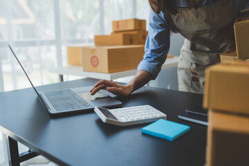 Small business start-up, SME owner, female entrepreneur working on packaging parcels. Receipt and check orders online to prepare boxes for sale to customers, online SME business concept.