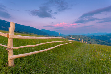 The wooden hedge on a green grass  hill in the Carpathian mountains in Ukraine in a summer evening sky with clouds.