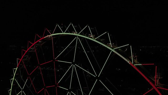 Aerial close-up: Ferris wheel at Aztlan Parque Urbano with Mexico City&acute;s skyline as background at night.