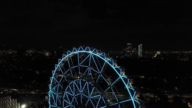 Aerial close-up of the new Ferris Wheel in Aztlan, Parque Urbano. Drone flying backwards slowly while revealing the skyline in Mexico City.