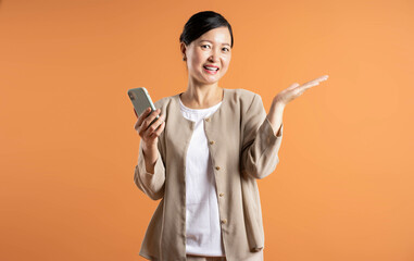 Portrait of middle age Asian woman using phone on brown background