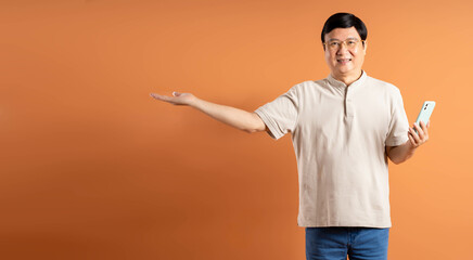 Portrait of middle-aged Asian man using phone on brown background