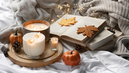 Autumn still life with candles, pumpkins, books and a knitted element.
