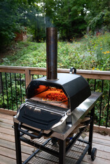 Portable pizza oven cooking a homemade pizza on a deck.