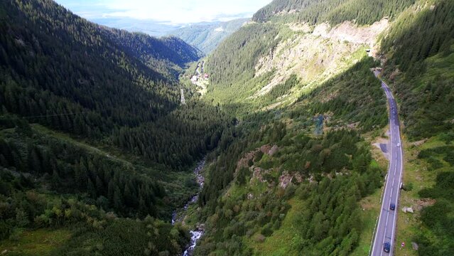 Drone descends above Transfagarasan Serpentine Road showcasing mountain river rushing through valley