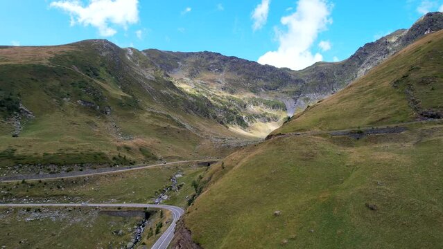 Drone descends along hillside as car drive along Transfagarasan Serpentine Road at midday