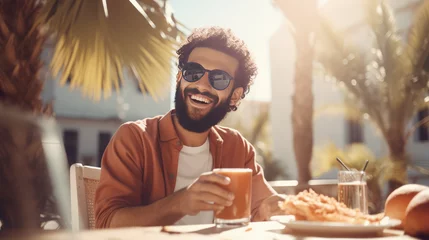 Foto op Plexiglas Smiling man holding glass of juice and sitting at cafe outdoors at summer © valgabir