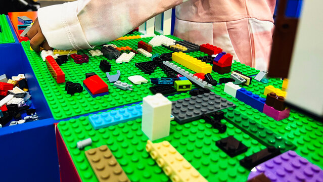Close up of the hands of an Asian girl in a pink dress arranging bricks on a Green Board.