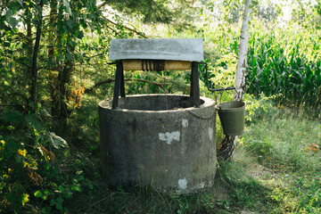 Old concrete well. Metal bucket. Metal chain pulley. Simple machine in forest. Deep water source.