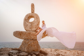 Woman sky stone. Lady stands on stone sculpture with ocean view. She is dressed in a white long...