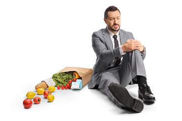 Businessman with a grocery bag sitting on the floor and holding his painful knee