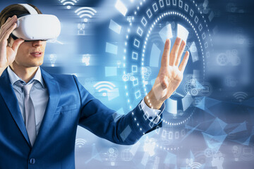 Young businessman with VR glasses using glowing digital business interface with cogwheels and icons on blurry office interior backdrop. Future, virtual reality, innovation and technology concept.