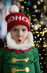child in an elf costume and a Santa hat makes faces. Emotion of surprise and delight. Christmas,...