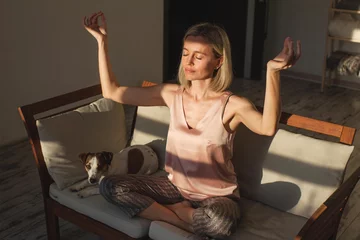 Poster mindful middle aged woman making mudra gesture sitting in lotus position on couch at home © Tatyana Gladskih