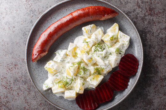Smoked sausage with potatoes in cream sauce with dill and boiled beets close-up on a plate on the table. Horizontal top view from above