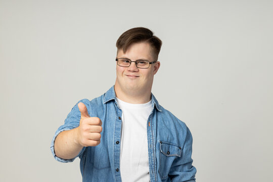A smiling young man with cerebral palsy in glasses, jeans and a white T-shirt poses for the camera. World Genetic Diseases Day concept - Powered by Adobe