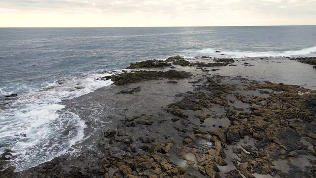 Dynamic aerial footage of El Bufadero de La Garita in Gran Canaria, where forceful ocean waves crash into rugged volcanic cliffs, creating spectacular water explosions and natural blowholes.