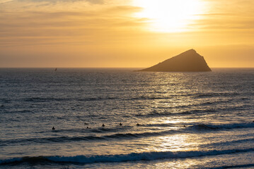Sunset over the Great Mewstone with surfers in the foreground at Wembury beach in Devon, UK.