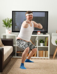 Fototapeta na wymiar Young handsome man in shorts and vest holds pink dumbbells in hand. Watch tv lessons single combats is practicing receptions of sensei one home fitness indoor training independent education remotely
