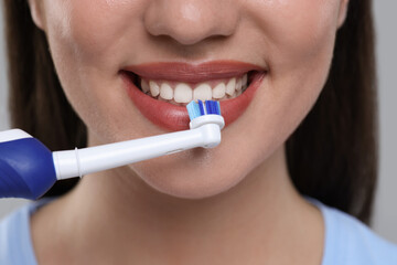 Woman brushing her teeth with electric toothbrush on light grey background, closeup