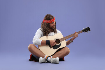 Stylish hippie man playing guitar on violet background