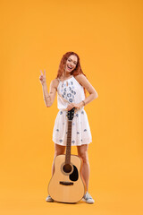 Beautiful young hippie woman with guitar showing V-sign on orange background