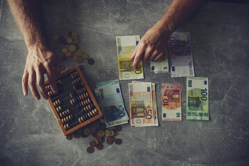 Man counting money on gray table with abacus and euro banknotes - obrazy, fototapety, plakaty