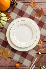 Above vertical photo of festive Thanksgiving family gathering evokes beauty of fall. Gilded tableware, classic cutlery, and autumnal decorations rest on a brown wooden backdrop, inviting text or ads