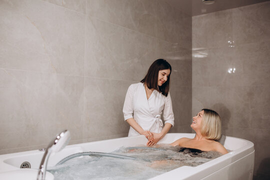 Young woman during hydromassage in beauty salon. Concept of body care and spa. Masseuse massages the girl in the bath with a jet of water. High quality photo