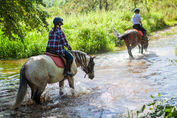 Horse ride, young girls riders, crossing a river, a stream on horseback, splashes from horse...