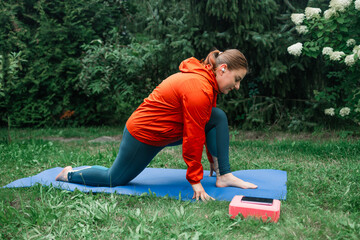Athletic 30s woman doing poses at yoga mat outdoors dressed in sport clothes alone in the park or forest in nature. High quality photo