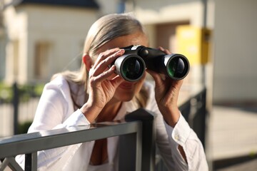 Concept of private life. Curious senior woman with binoculars spying on neighbours over fence...