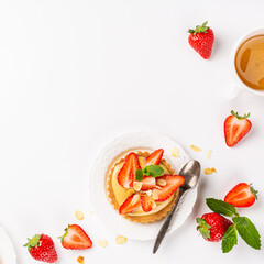 Summer composirion with strawberry mini cake tartlet with vanilla custard, sprinkled with almond flakes and mint over white. Concept of high tea healthy sweet pastries with copy space