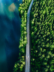 Aerial view of road with cars between green forest and blue lake in Finland
